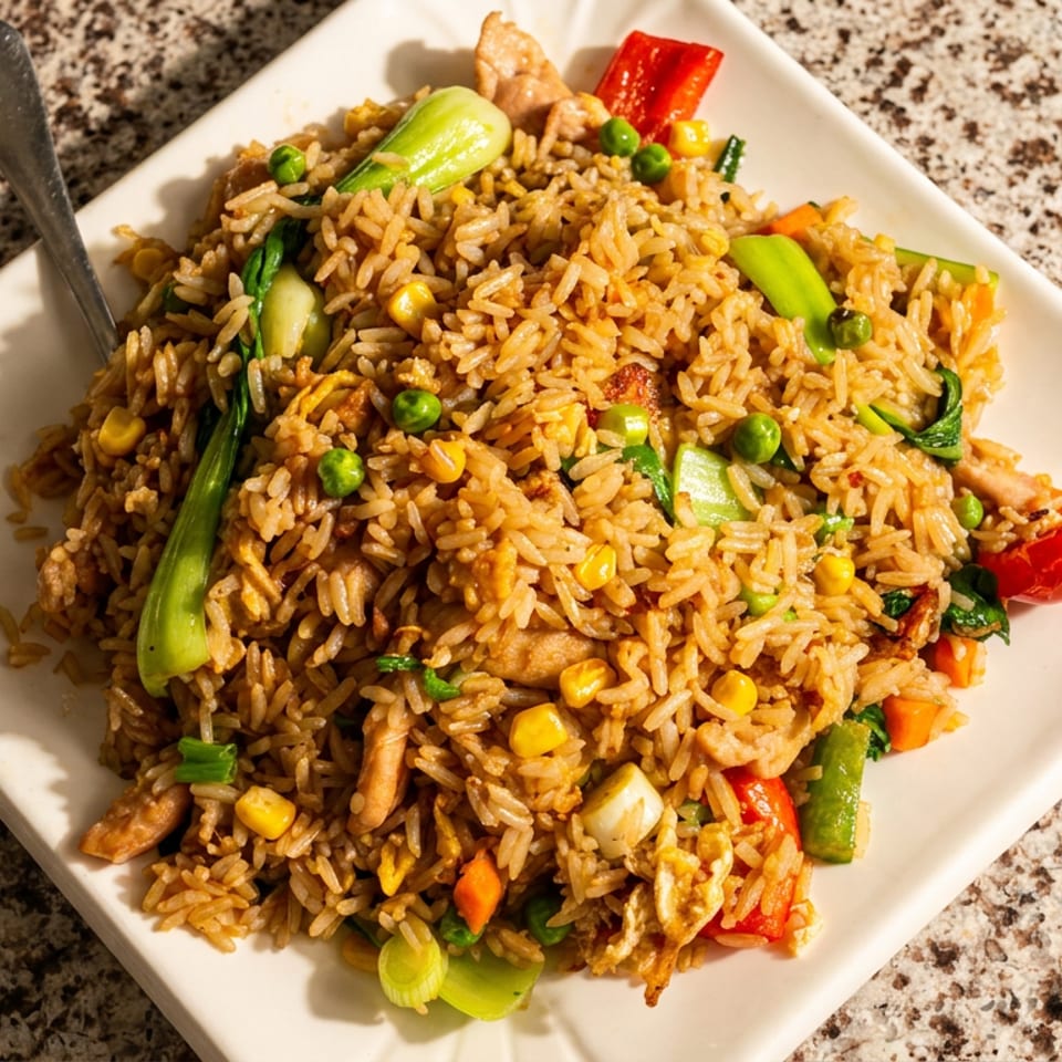 Plate of vegetable fried rice with peas, corn, carrots, bok choy, peppers, and chicken on a speckled countertop.