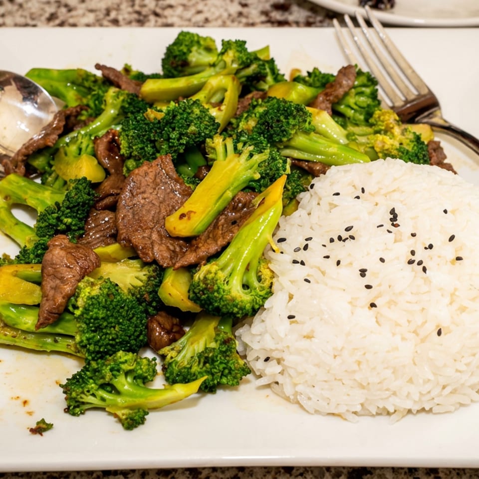 Beef and broccoli stir-fry with mixed vegetables and sesame-topped white rice on a square plate.