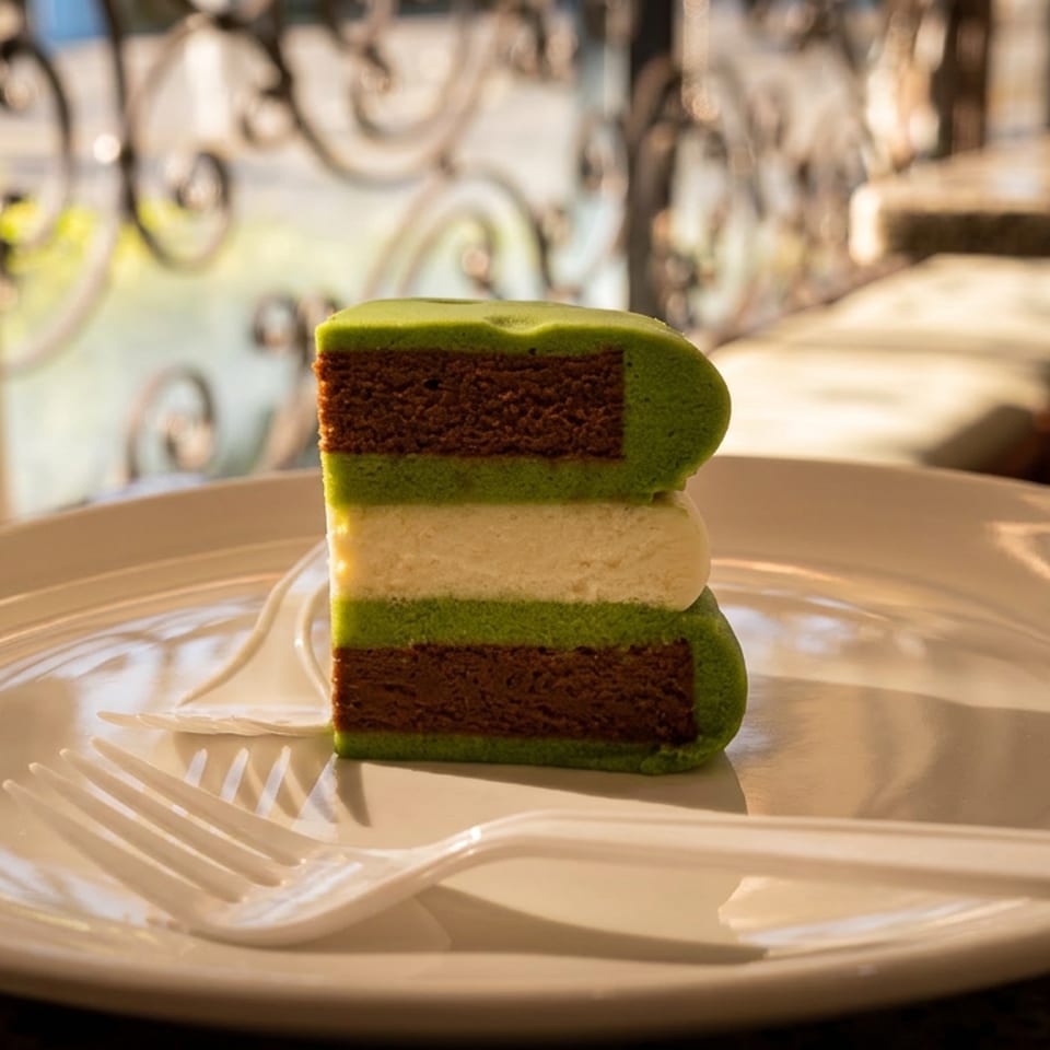 Slice of green and chocolate layered cake with creamy filling on a white plate beside a plastic fork.